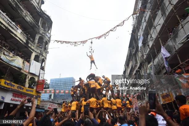 Indian young Hindu devotee hangs from a rope after breaking a dahi-handi suspended in the air as a human pyramid collapses beneath him during...