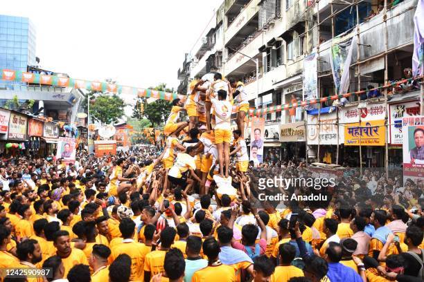 Indian young Hindu devotee hangs from a rope after breaking a dahi-handi suspended in the air as a human pyramid collapses beneath him during...