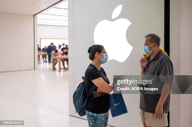 Couple stands in front of the American multinational technology company Apple logo and store in Hong Kong.