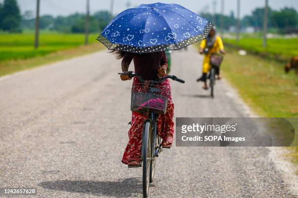 Woman holding an umbrella pedals on her bicycle along the highway on a hot summer day at Baniyani in Jhapa District.