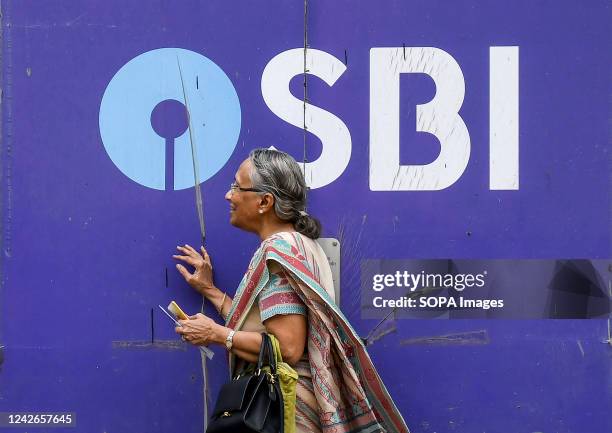 Woman walks past a logo of State Bank of India at Currey road branch in Mumbai. State Bank of India is a fortune 500 company and one of the most...