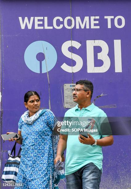 People walk past a logo of State Bank of India at Currey road branch in Mumbai. State Bank of India is a fortune 500 company and one of the most...