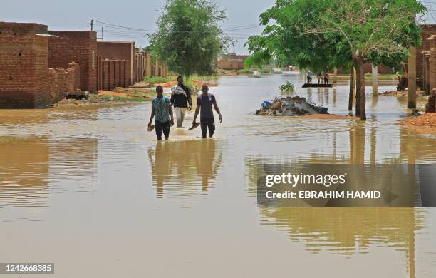 People wade through flood water in Managil city in al-Gezira state, around 250Km south of the capital, on August 23, 2022. - Sudan declared a state...