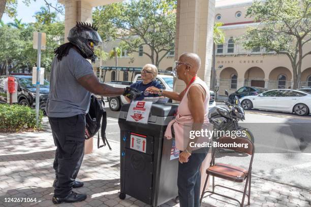 An election official hands an "I Voted" sticker to a voter dropping off a mail-in ballot outside of a polling location in Saint Petersburg, Florida,...