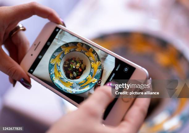 August 2022, Berlin: A woman takes a picture with her smartphone of the dish "Drop it like it's hot" at the restaurant "Coccodrillo" in...