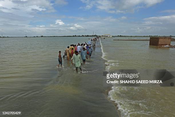 Stranded people wade through a flooded area after heavy monsoon rainfall in Rajanpur district of Punjab province on August 25, 2022. - Figures from...