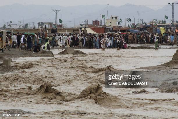People wade through flooded mud water after heavy monsoon rainfall in the border town of Chaman in Balochistan province on August 25, 2022. - Figures...
