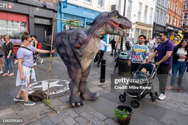 Tourists and domestic visitors are delighted by a street performer dressed up as a Tyrannosaurus Rex having pictures take with them for money in...