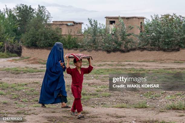Burqa-clad Afghan woman walks with a boy at Bagram district in Parwan province on August 25, 2022.
