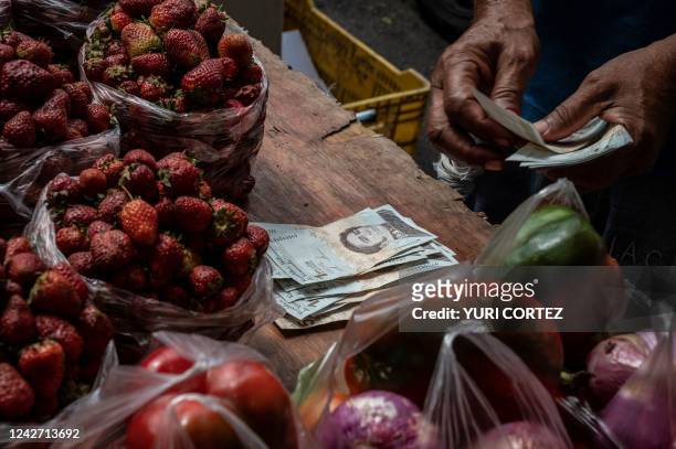 Fruit and vegetable vendor counts money in bolivar and dollar bills while waiting for customers at the Quinta Crespo municipal market in Caracas on...