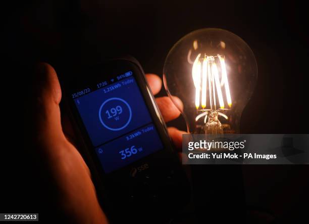 Handheld SSE smart meter for household energy usage is held next to an energy-efficient LED light bulb. Families across Great Britain will find out...
