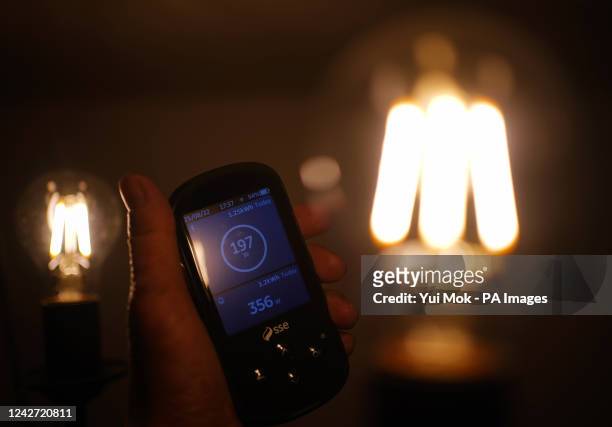 Handheld SSE smart meter for household energy usage is held next to an energy-efficient LED light bulb. Families across Great Britain will find out...