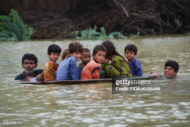 Man along with a youth use a satellite dish to move children across a flooded area after heavy monsoon rainfalls in Jaffarabad district, Balochistan...