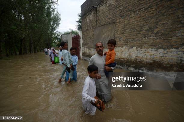 People walk through floodwaters as flood water entered houses and damaged standing crops in Dagai Mukram Khan, Peshawar, Pakistan on August 26, 2022....