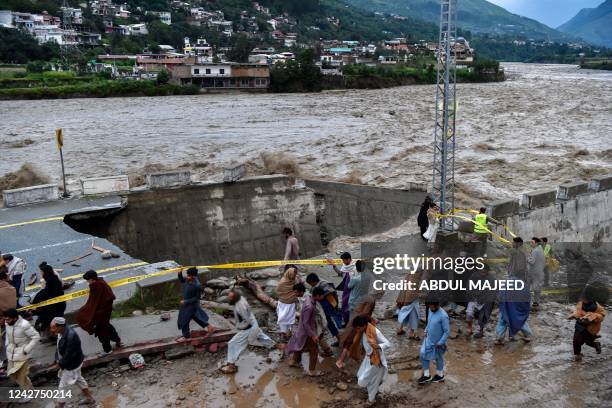 People gather in front of a road damaged by flood waters following heavy monsoon rains in Madian area in Pakistan's northern Swat Valley on August...