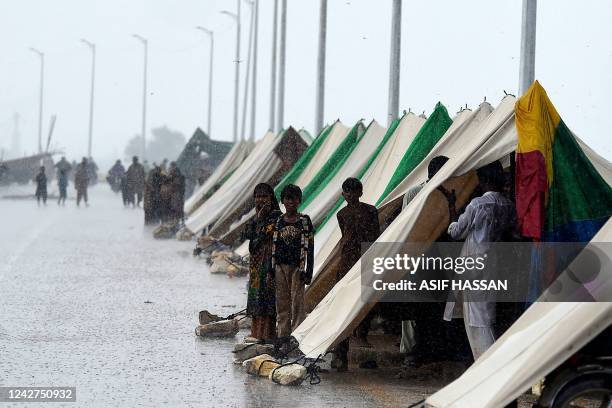 People who fled their flood hit homes stand outside temporary tents set along a road during a heavy monsoon rainfall in Sukkur of Sindh province, on...