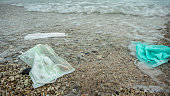 Coronavirus polluting environment. Waves wash up old medical mask waste