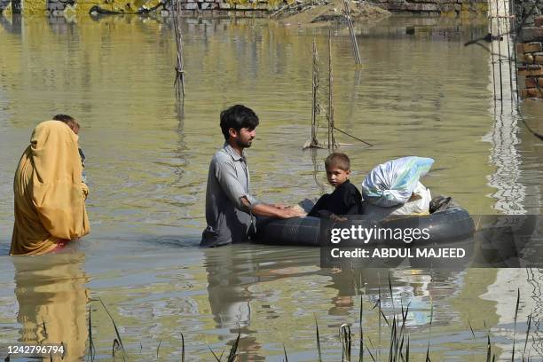 Family wades through a flood hit area following heavy monsoon rains in Charsadda district of Khyber Pakhtunkhwa on August 29, 2022. - The death toll...