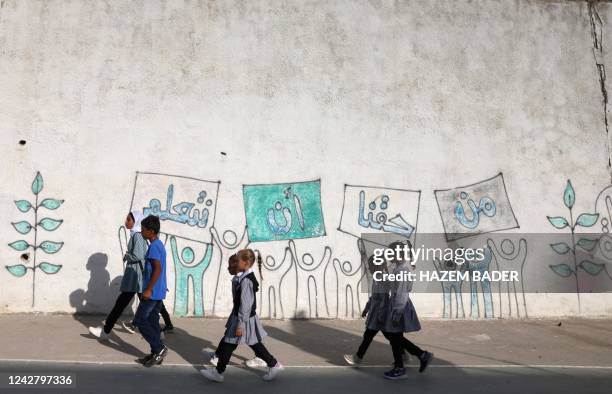 Palestinian pupils walk past a mural depicting youths lifting placards with an Arabic inscription which reads "we have the right to learn", as they...