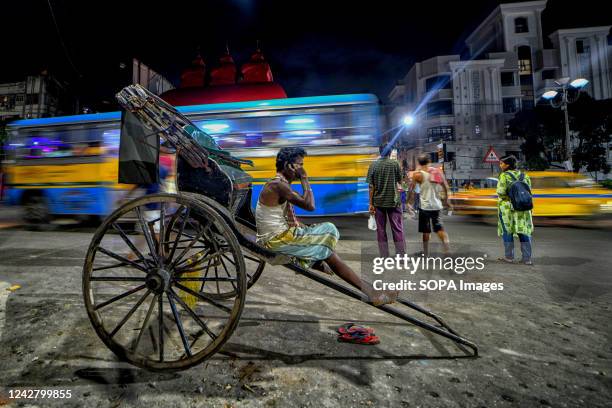 Street rickshaw puller seen sitting along the main road while waiting for customers .