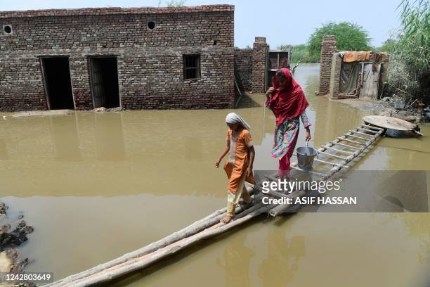 Flood affected people walk on a temporary bamboo path near their flooded house in Shikarpur of Sindh province on August 29, 2022. - The death toll...