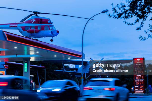 August 2022, North Rhine-Westphalia, Leverkusen: Cars refuel and drive past a gas station with an old helicopter on its roof and a historic Antonov...