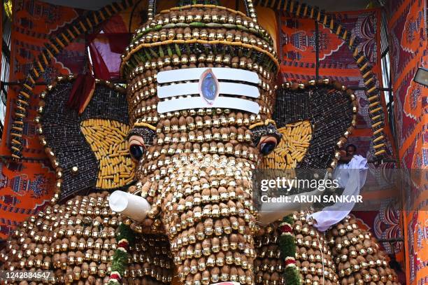 Man removes a cloth to unveil a 30-feet statue of Elephant headed hindu god Ganesha made Metal pots, coconut ,corn and sugarcane at a place worship...