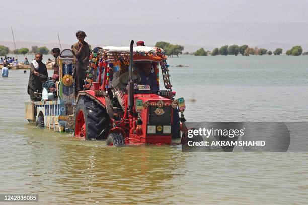 Displaced people who fled from flood-hit areas sit on a tractor to cross a flooded area at Sehwan in Sindh province on August 31, 2022. - Army...