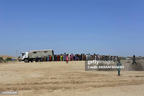 Displaced people who fled from flood-hit areas stand in a queue to receive relief food packets from Pakistan's Rangers at Sehwan in Sindh province on...