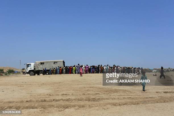 Displaced people who fled from flood-hit areas stand in a queue to receive relief food packets from Pakistan's Rangers at Sehwan in Sindh province on...
