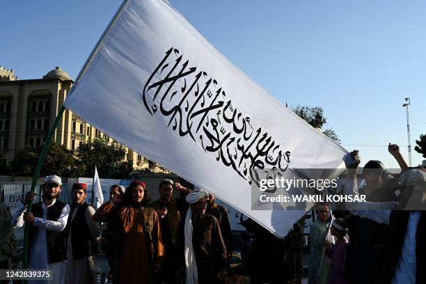 Taliban fighters hold a Taliban flag as they celebrate the first anniversary of the withdrawal of US-led troops from Afghanistan, near the former US...