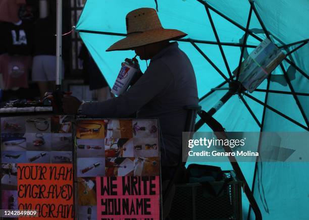 Miguel Angel quenches his thirst under the hot sun while waiting for customers at Your Name On A Grain Of Rice on the first day of a heatwave on the...