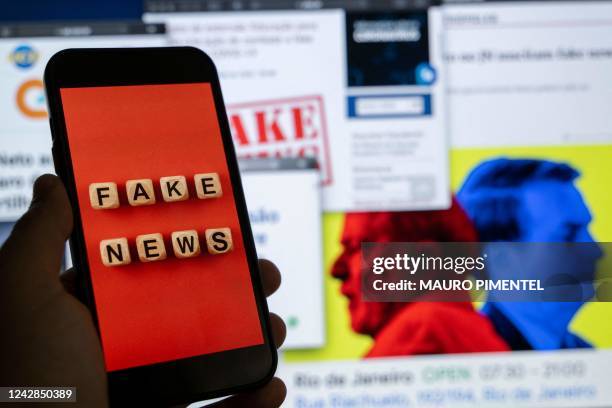 This illustration picture shows a smart phone screen displaying the phrase "Fake News" in front of a desktop screen showing several news and research...