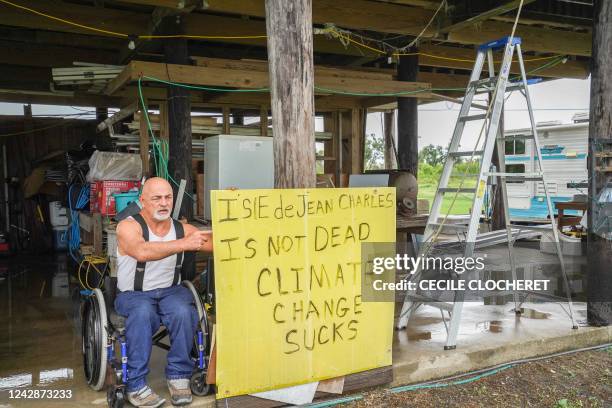 Chris Brunet poses outside his house next to a sign that reads "The Isle of Jean Charles is not dead Climate change stinks" on the Isle of Jean...