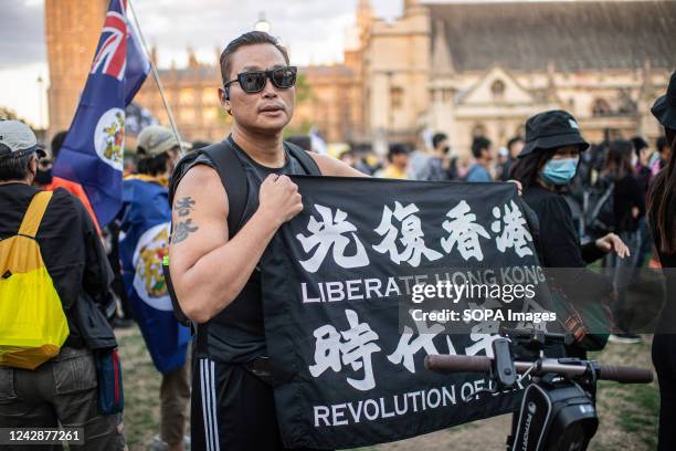 Man poses with a banner that says "Liberate Hong Kong, Revolution of our Times" and shows his Hong Kong protest tattoo, which says "Go Hong Kong,"...