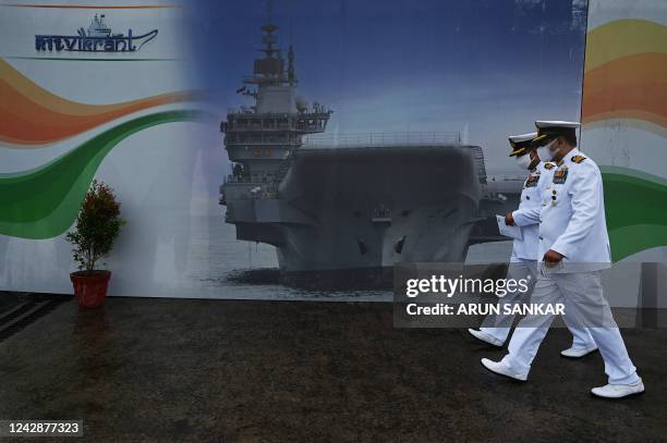 Indian Navy officers walk past a hoarding with a picture of the the Indian indigenous aircraft carrier INS Vikrant during its commissioning at Cochin...