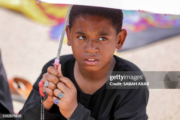 Young Iraqi holds an umbrella as supporters of Iraq's Shiite cleric Moqtada Sadr listen to the sermon following the Friday prayer in Sadr City in...