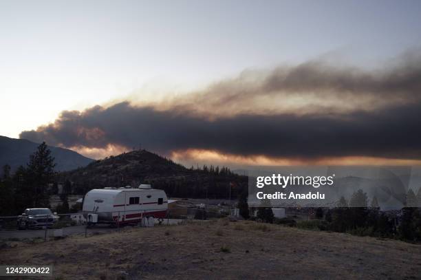 Smoke from the Mountain fire can be seen in the background as the remnants of an old mill building smolders in the foreground in Weed on Tuesday...