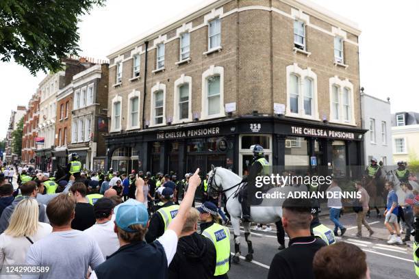 West Ham United's fans gesture as they walk past The Chelsea Pensioner pub escorted by police officers on their way to attend the English Premier...