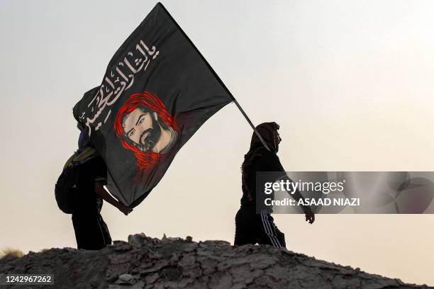 Shiite Muslim pilgrim marches with a flag bearing the image of Imam Hussein and the Arabic slogan "Yalatharat al-Hussein" while en route to Karbala...