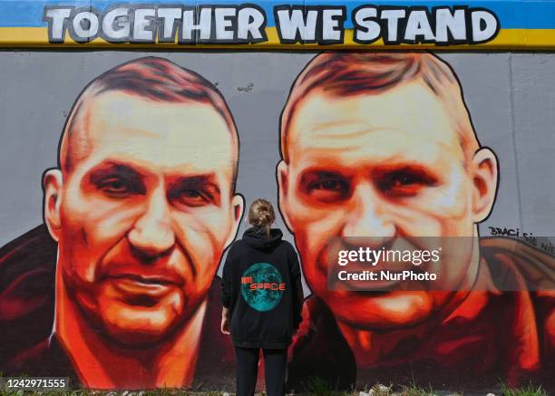 Young woman looks at a pro-Ukrainian mural entitled 'Together We Stand' futuring Wladimir and Vitali Klitschko, created by Polish artist TUSE . More...