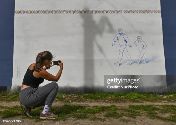 Young woman is taking a photo of a pro-Ukrainian mural created by Polish artist Katarzyna Witek More than 25 anti-war and pro-Ukrainian murals were...