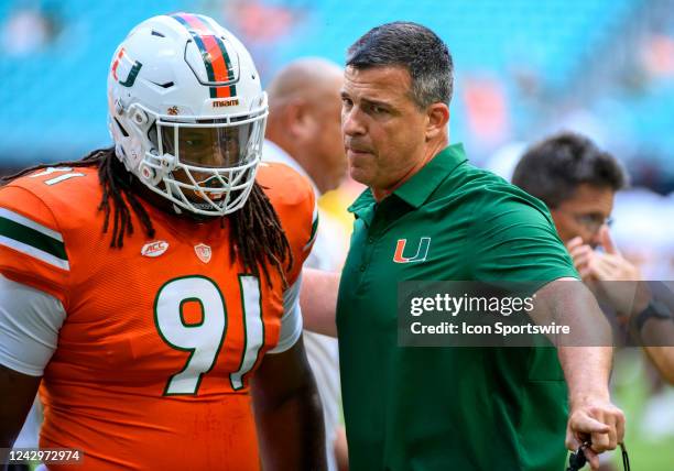 Miami head coach Mario Cristobal talks with Miami defensive line Jordan Miller on the field before the start of the college football game between the...