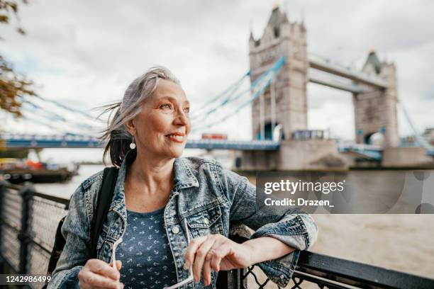 senior female tourist with blue eyes in london near tower bridge, traveling to uk after pandemic - london tourist stock pictures, royalty-free photos & images