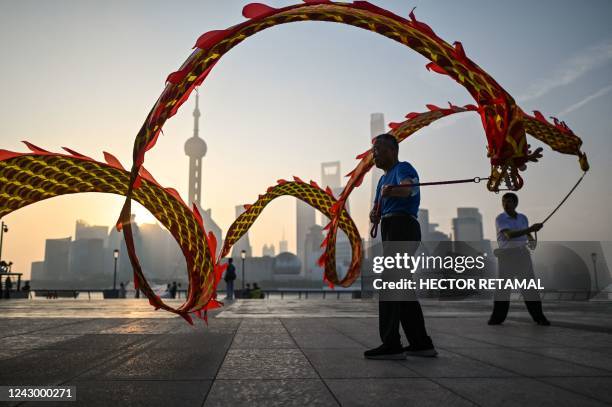 Men twirl dragon streamers on the Bund promenade along the Huangpu River during sunrise in Shanghai on September 7, 2022.