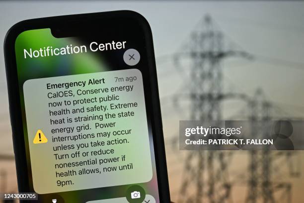 Photo illustration shows a background of electric power infrastructure with an Apple iPhone showing an Emergency Alert notification from CalOES...