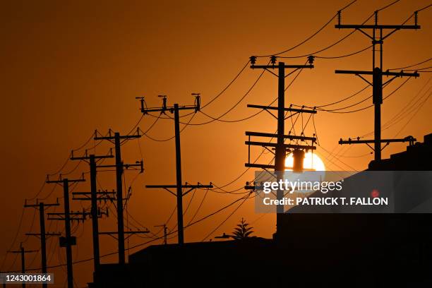 The sun sets behind power lines near homes during a heat wave in Los Angeles, California on September 6, 2022. - A blistering heat wave is baking the...