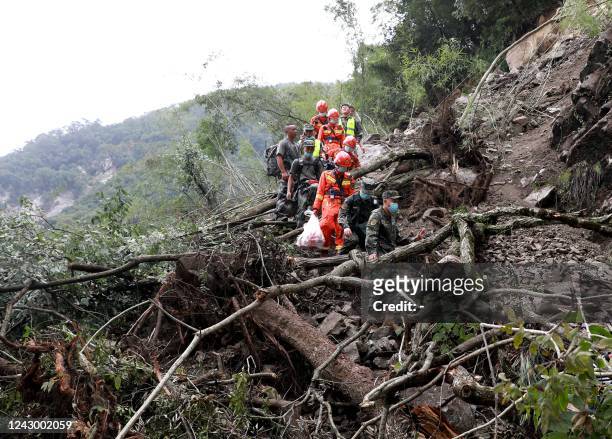 This photo taken on September 6, 2022 shows rescuers walking past uprooted trees from a landslide as they head to an earthquake-affected area...