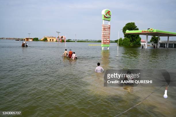 Internally displaced people wade through floodwaters to return home after heavy monsoon rains in Dadu district, Sindh province on September 7, 2022.
