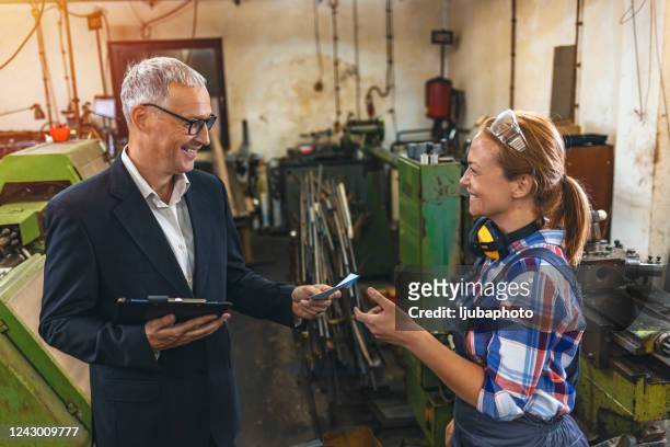 manlig handledare står stolt i fabriken och ger löner till sin kvinnliga medarbetare - staff benefits corporate bildbanksfoton och bilder